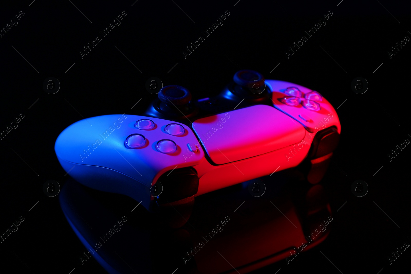 Photo of Wireless game controller on black mirror surface in neon lights