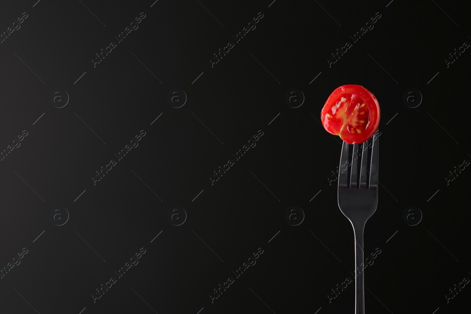 Photo of Fork with half of cherry tomato on black background