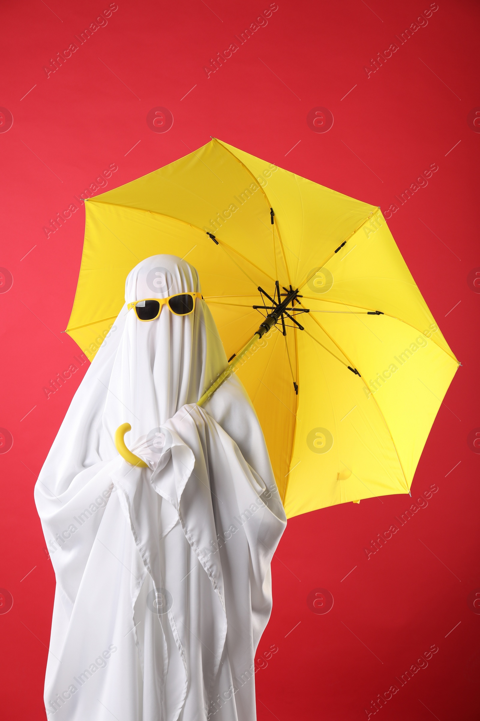 Photo of Person in ghost costume and sunglasses holding yellow umbrella on red background