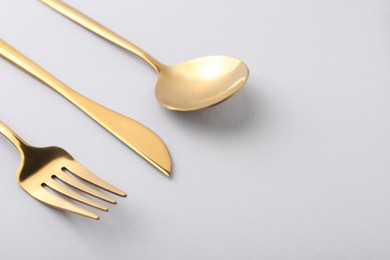 Stylish golden cutlery set on gray background, closeup. Space for text