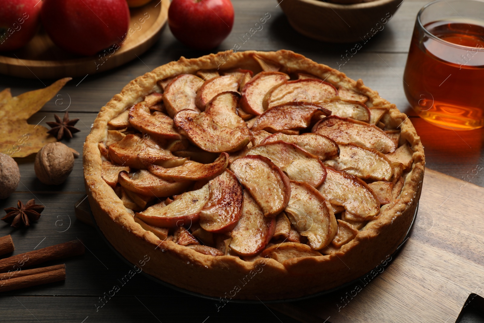 Photo of Delicious apple pie, ingredients and cup of tea on wooden table