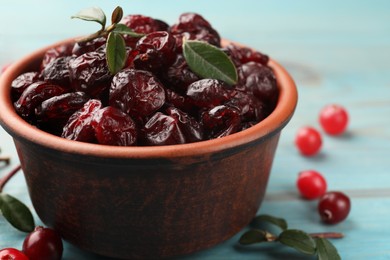 Photo of Tasty dried cranberries in bowl, fresh ones and leaves on table, closeup