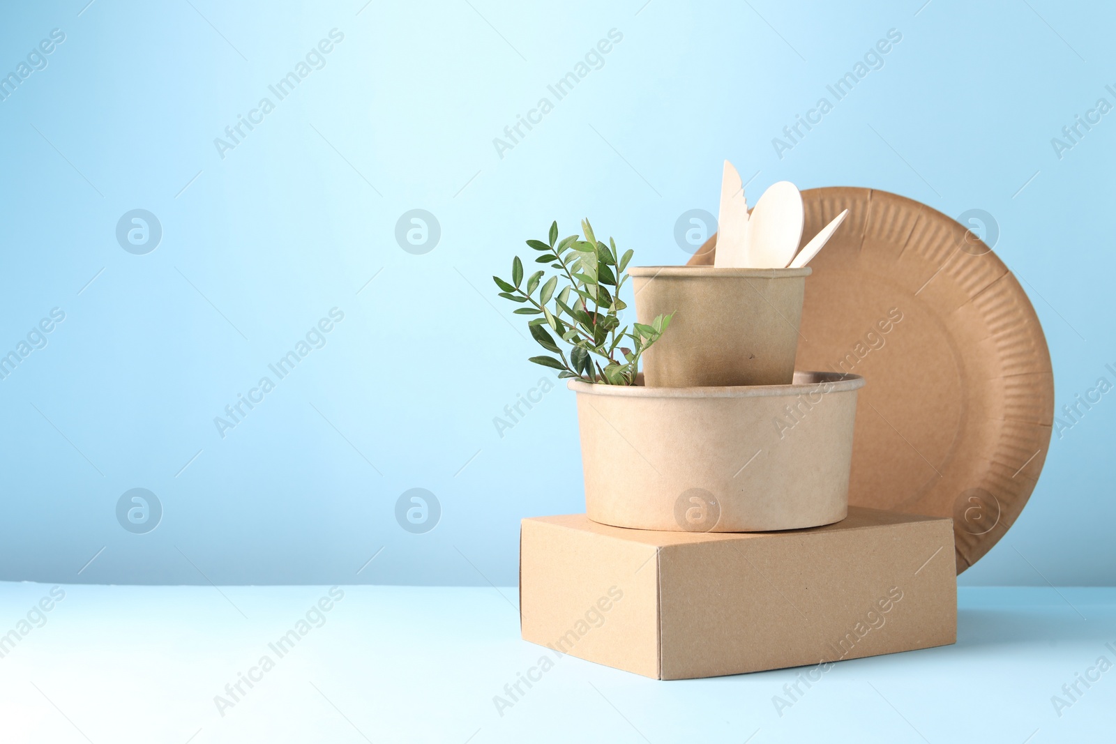 Photo of Eco friendly food packaging. Paper containers, tableware and green twig on white table against light blue background, space for text