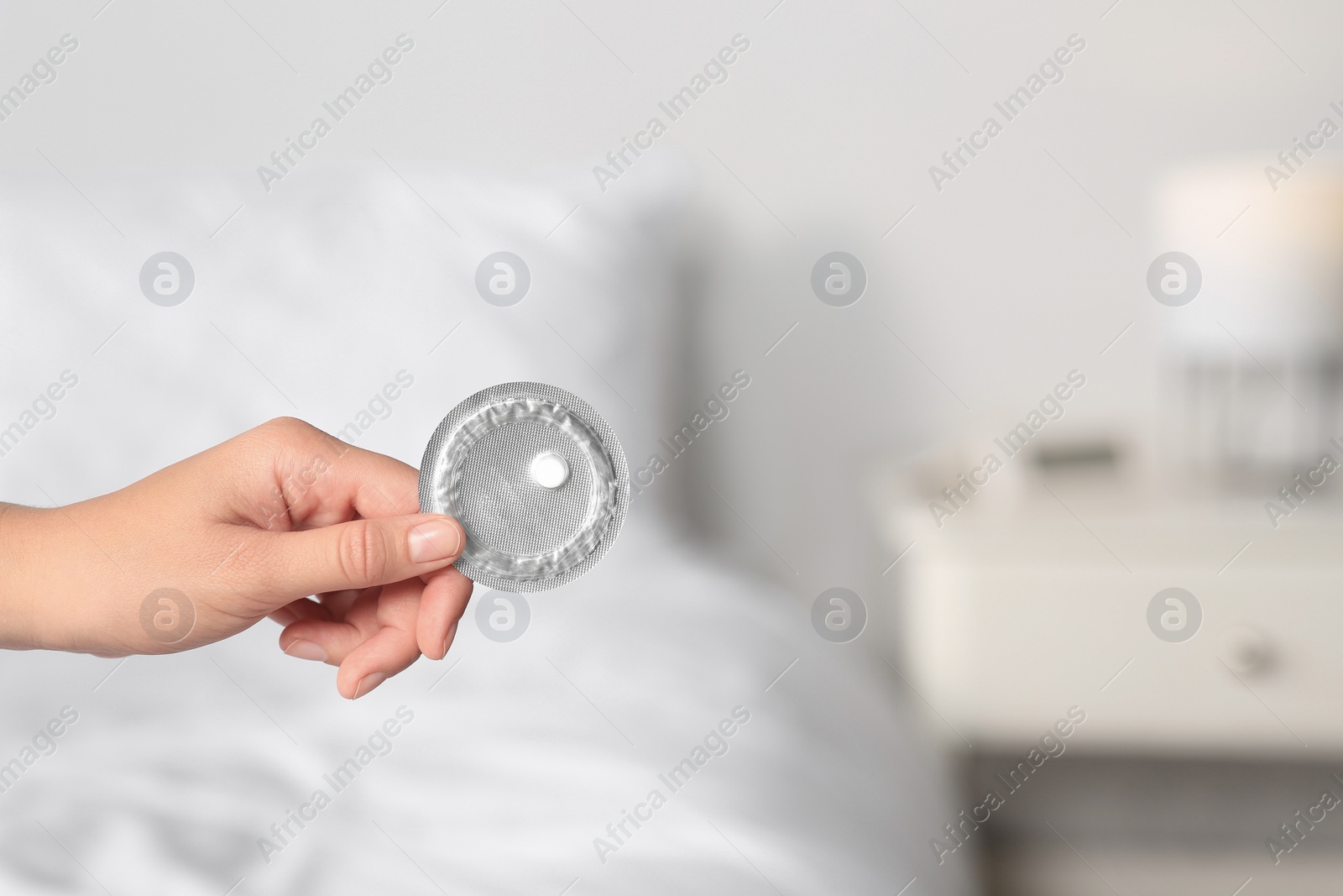 Photo of Woman holding blister of emergency contraception pill against blurred background, closeup. Space for text