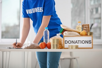 Photo of Female volunteer listing food products from donation box indoors