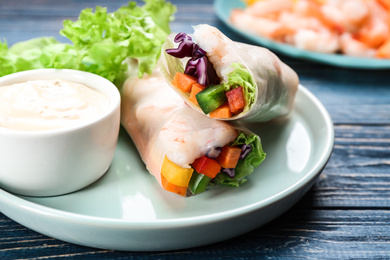 Photo of Delicious rolls wrapped in rice paper served on blue wooden table, closeup