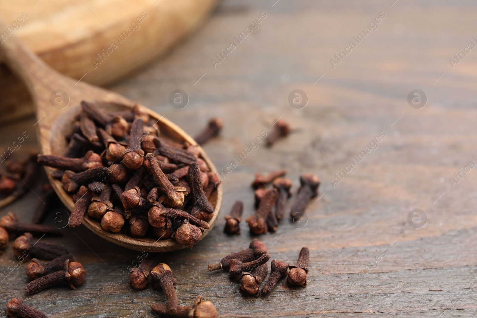 Photo of Spoon with aromatic cloves on wooden table, closeup. Space for text