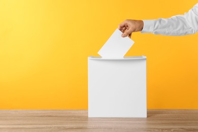 Photo of Man putting his vote into ballot box on yellow background, closeup. Space for text