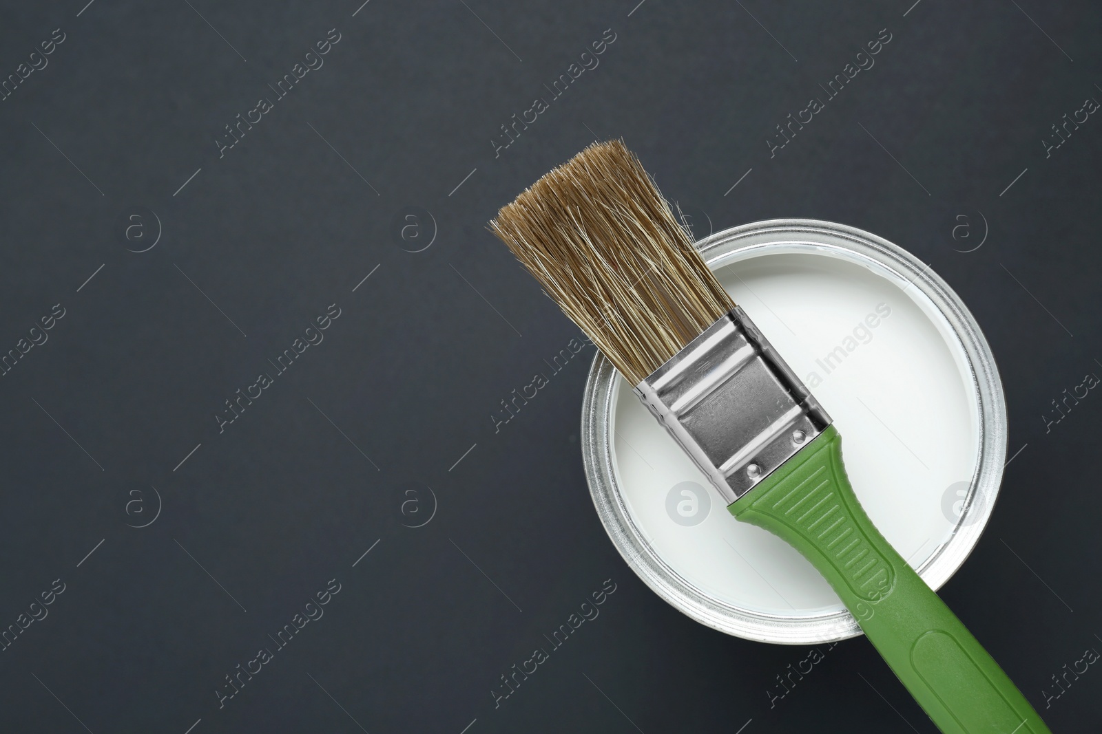 Photo of Can of white paint with brush on black background, top view. Space for text