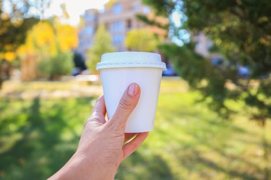 Photo of Woman holding cardboard cup with coffee in park, closeup
