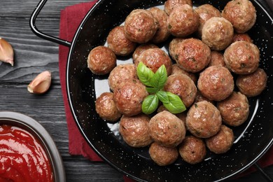 Photo of Tasty cooked meatballs with basil on black wooden table, flat lay