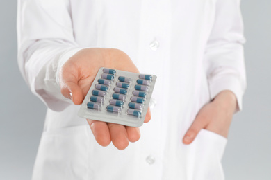 Professional pharmacist with pills on light grey background, closeup