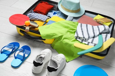 Photo of Open suitcase with stylish clothes, accessories, sport equipment and shoes on floor. Summer vacation