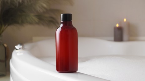 Red bottle of bubble bath on tub indoors, space for text