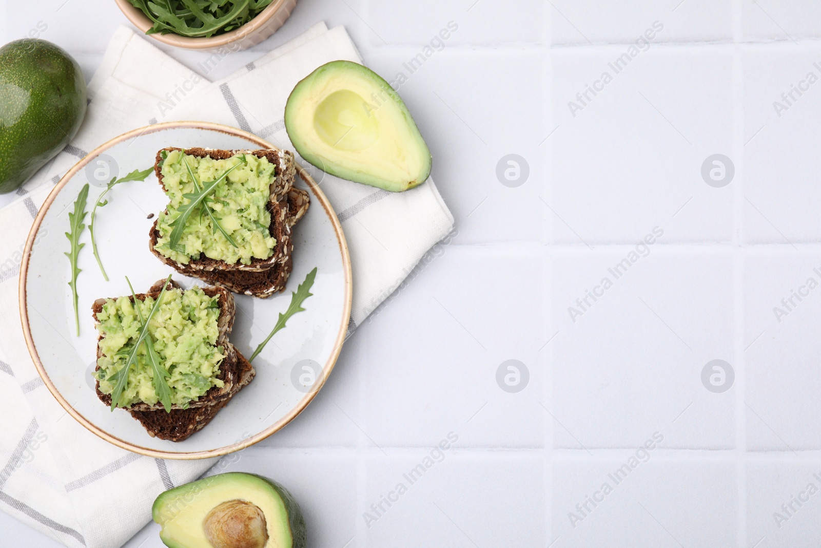 Photo of Delicious sandwiches with guacamole, arugula and avocados on white tiled table, flat lay. Space for text