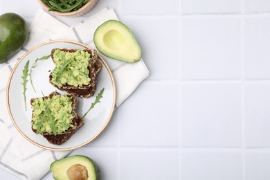 Photo of Delicious sandwiches with guacamole, arugula and avocados on white tiled table, flat lay. Space for text
