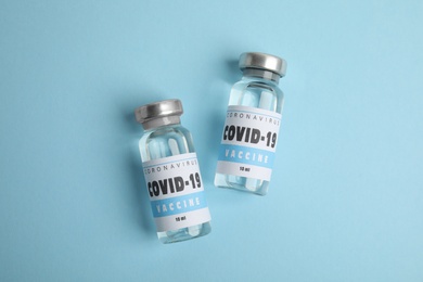 Photo of Vials with coronavirus vaccine on light blue background, flat lay