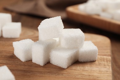 Photo of Refined sugar cubes with wooden board on table, closeup