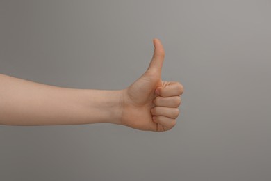 Photo of Woman showing thumb up on grey background, closeup