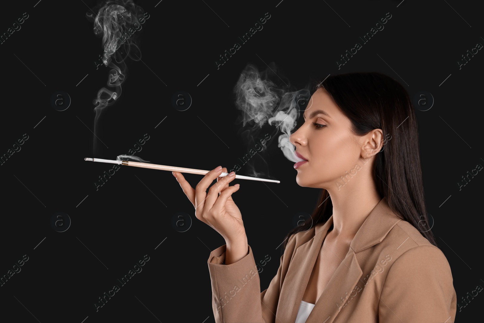 Photo of Woman using long cigarette holder for smoking on black background