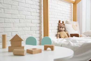 Photo of Toy deer on bed near white brick wall. Children's room interior design