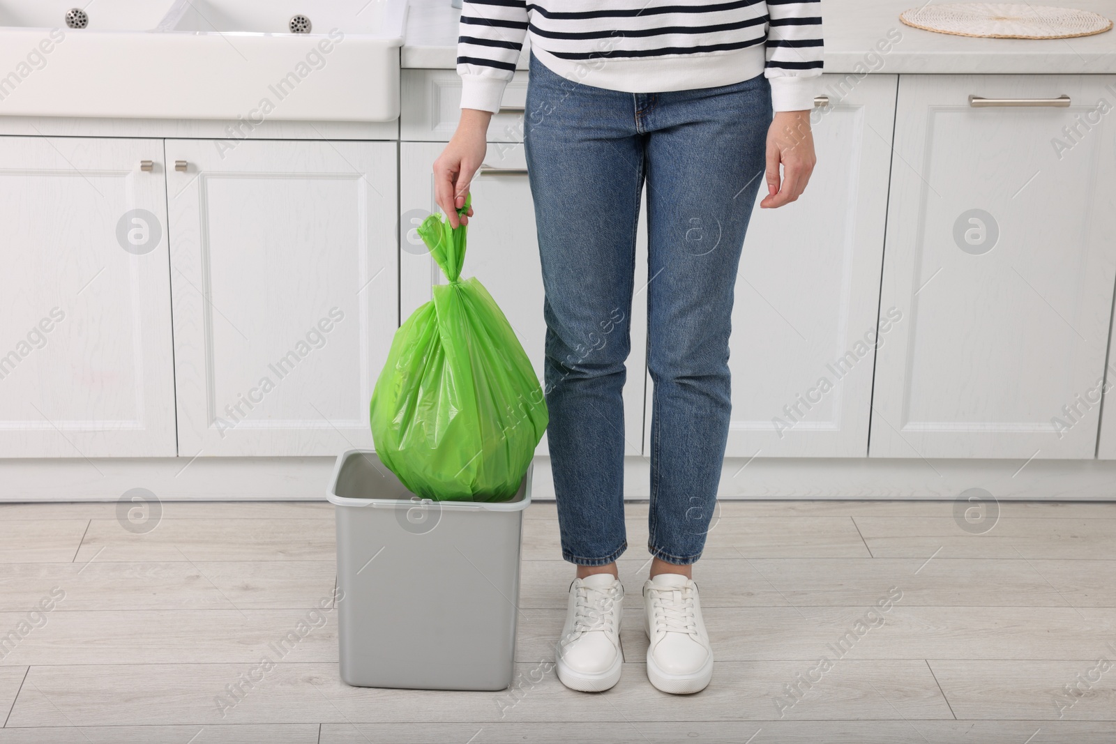 Photo of Woman taking garbage bag out of trash bin in kitchen, closeup