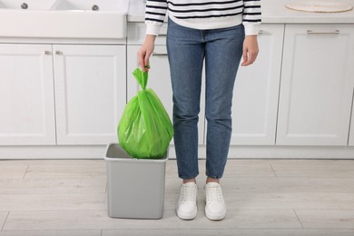 Photo of Woman taking garbage bag out of trash bin in kitchen, closeup