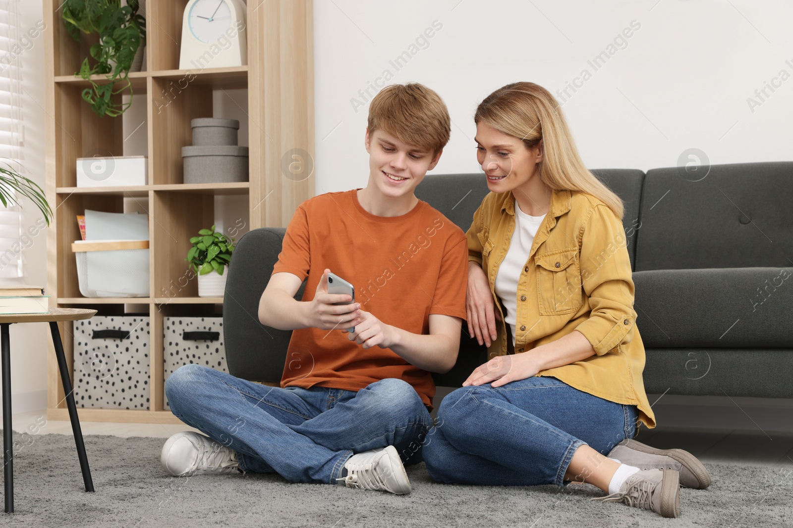 Photo of Happy mother and her teenage son with phone spending time together on floor at home