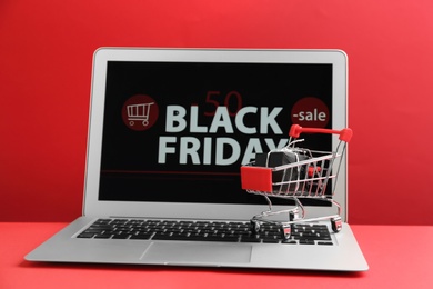 Photo of Laptop with Black Friday announcement, small shopping cart and gift on red background