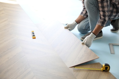 Worker installing laminated wooden floor indoors, closeup