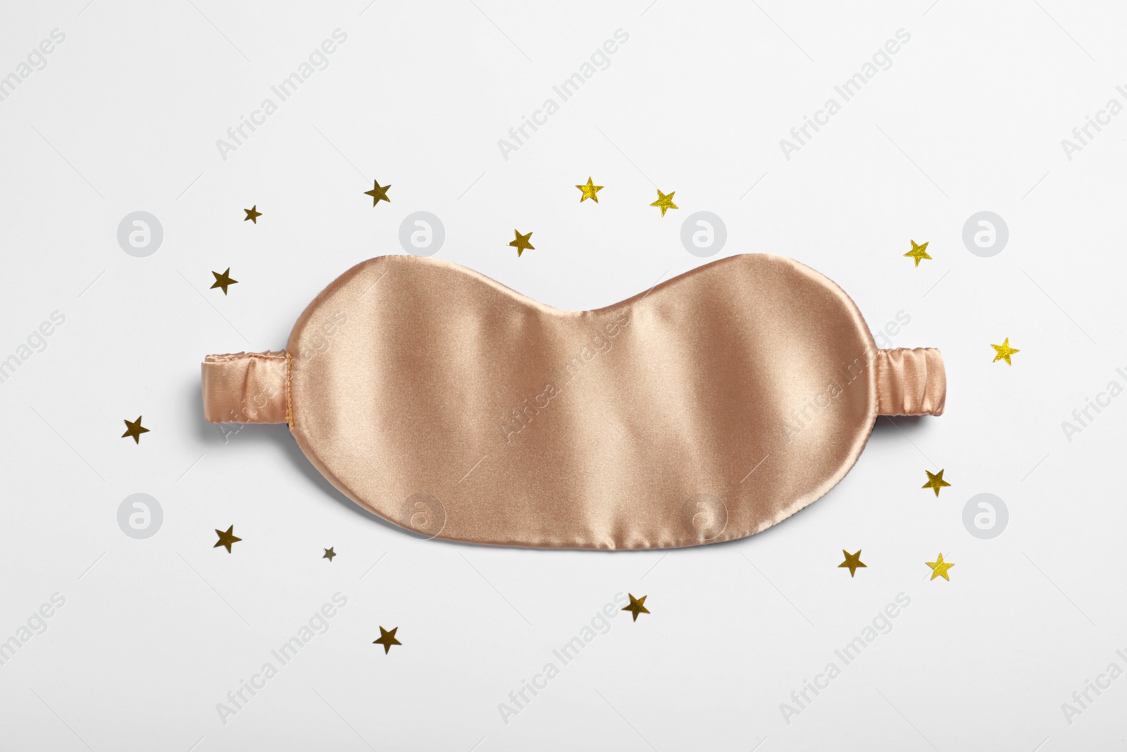 Photo of Beige sleeping mask and glitter on white background, top view. Bedtime accessory