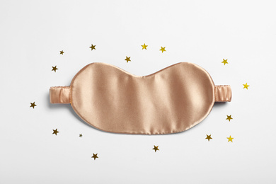 Photo of Beige sleeping mask and glitter on white background, top view. Bedtime accessory