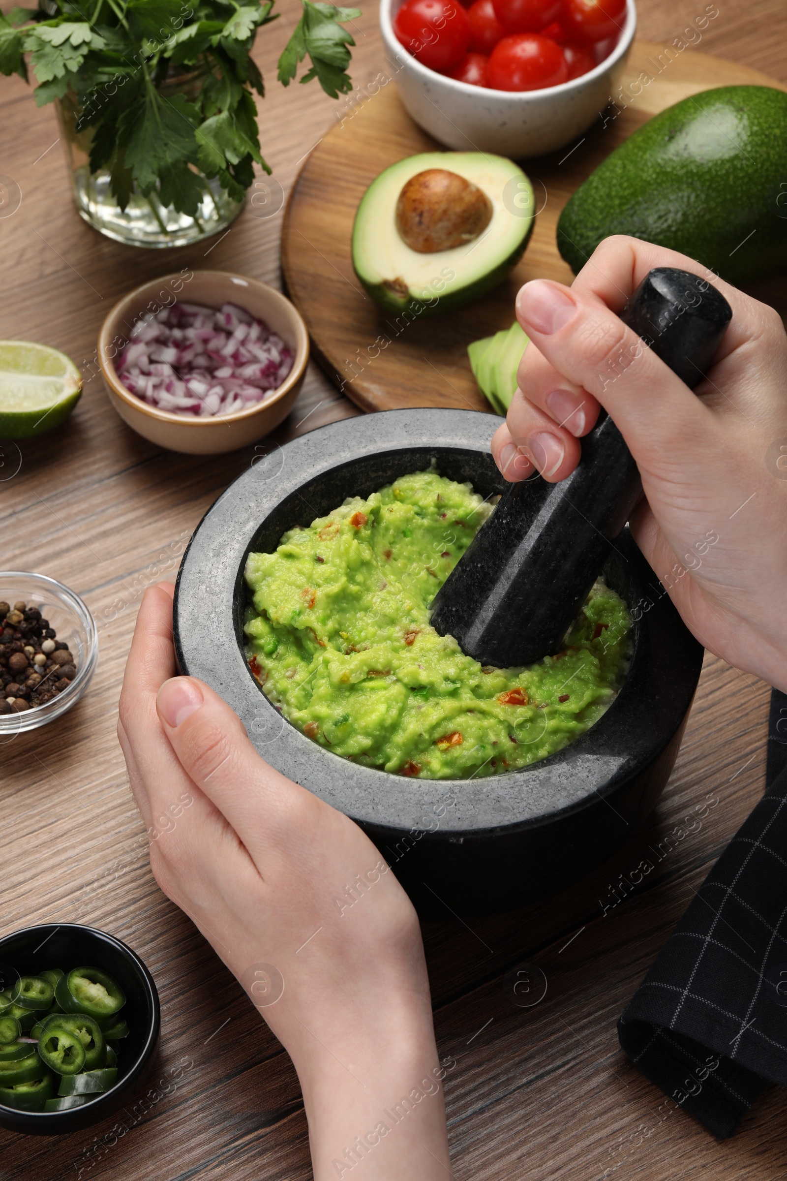 Photo of Woman preparing delicious guacamole at wooden table, closeup