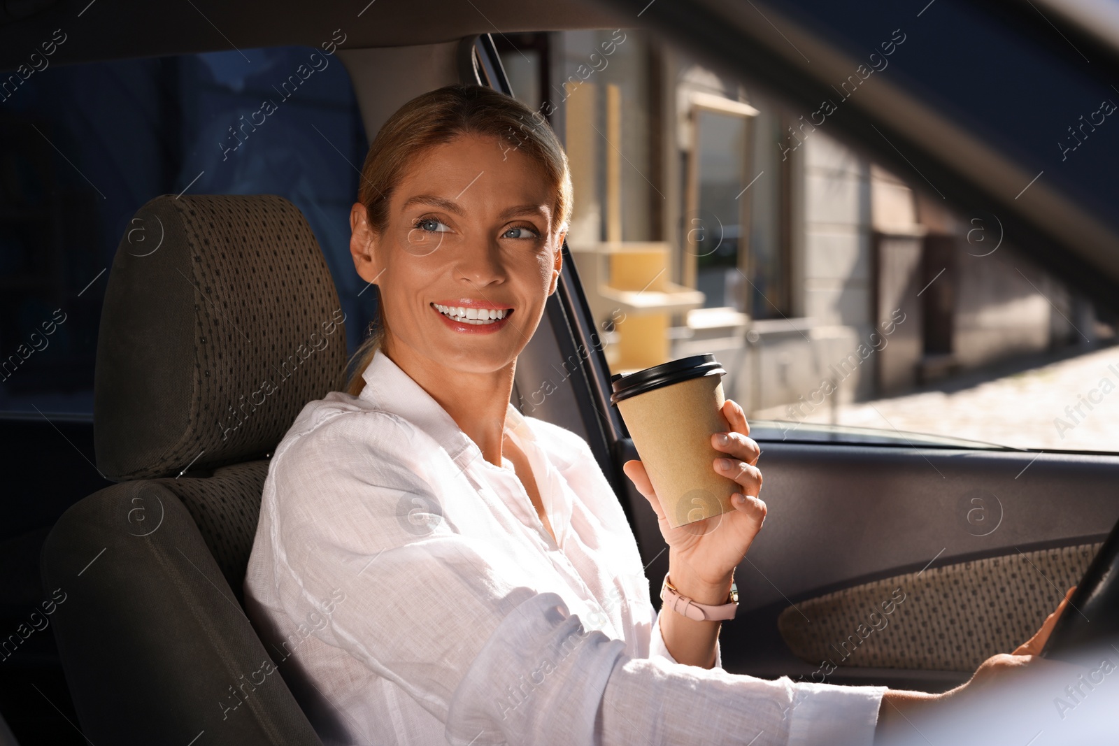 Photo of Coffee to go. Happy woman with paper cup of drink in car