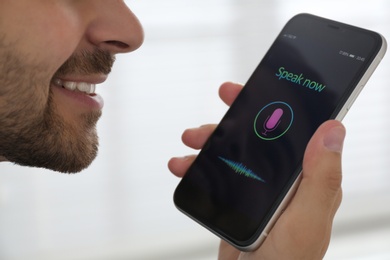 Young man using voice search on smartphone indoors, closeup
