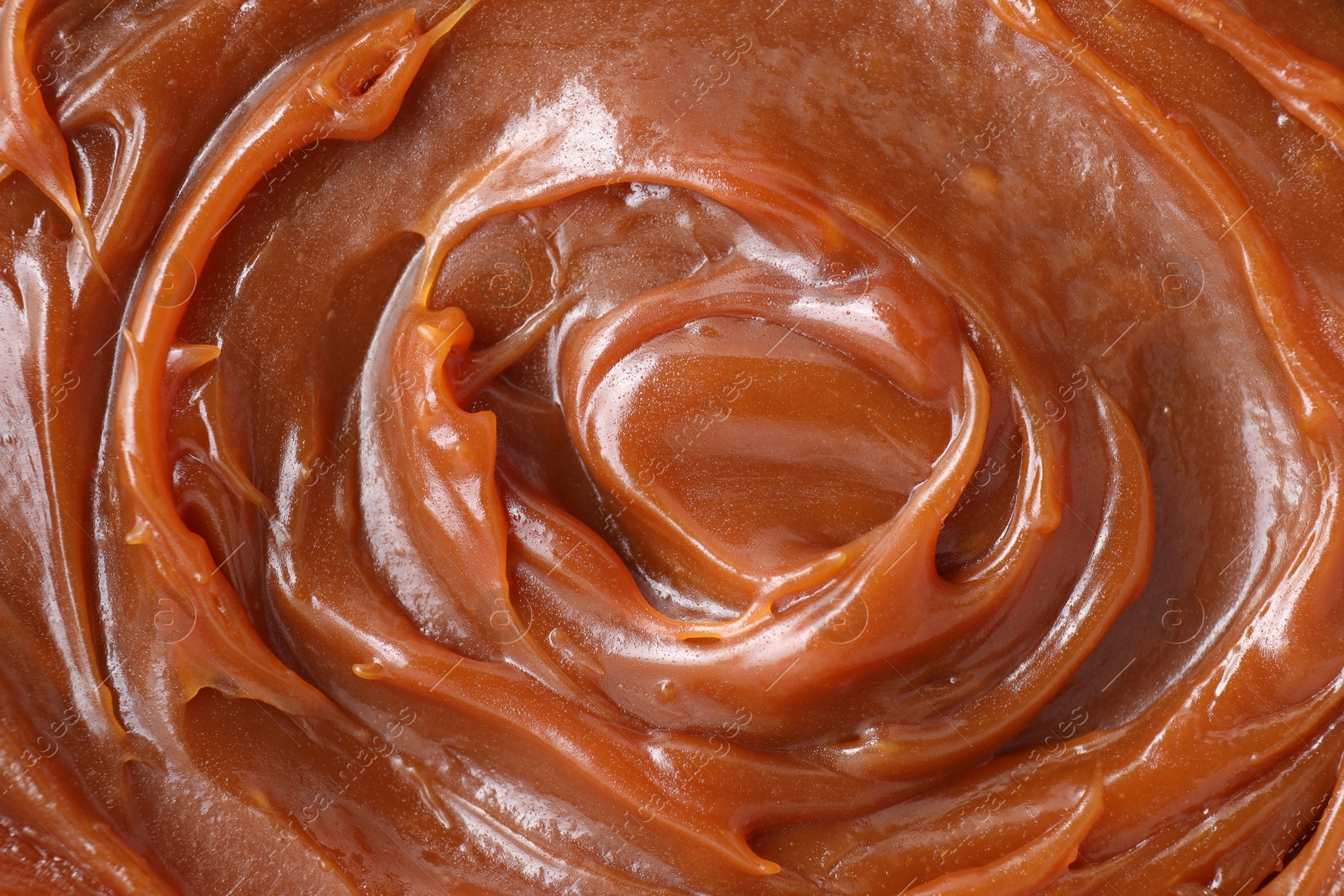 Photo of Tasty sweet caramel sauce as background, top view