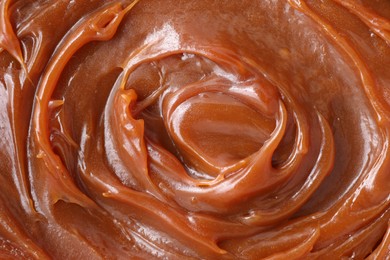 Tasty sweet caramel sauce as background, top view