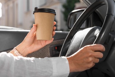 Coffee to go. Woman with paper cup of drink driving her car, closeup
