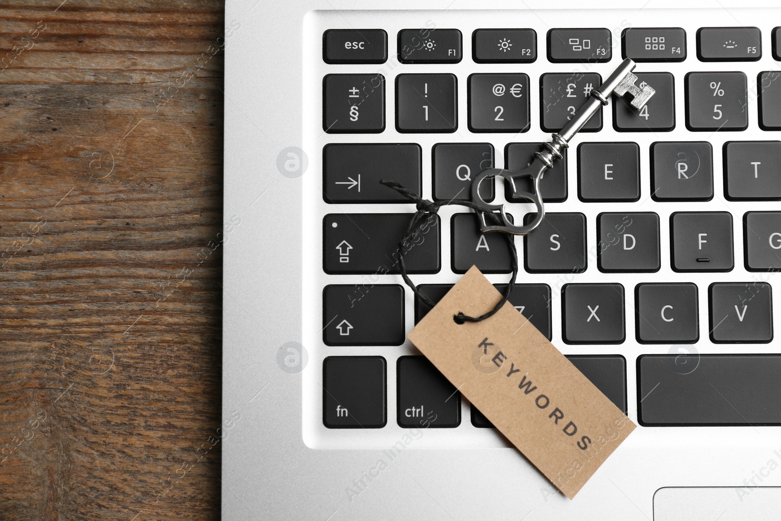 Photo of Laptop, vintage key and tag with word KEYWORDS on wooden table, top view