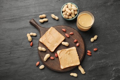 Photo of Tasty peanut butter sandwiches and peanuts on dark gray table, flat lay