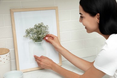 Photo of Happy woman with flowers and silicone vase attached to picture frame's glass on countertop in kitchen