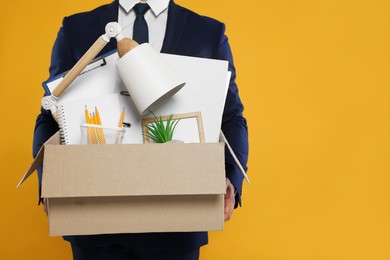 Photo of Unemployed man with box of personal office belongings on orange background, closeup. Space for text