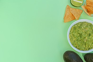 Delicious guacamole, avocados, lime and nachos on light background, flat lay. Space for text