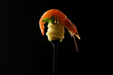 Fork with tasty pasta, shrimp and basil on black background