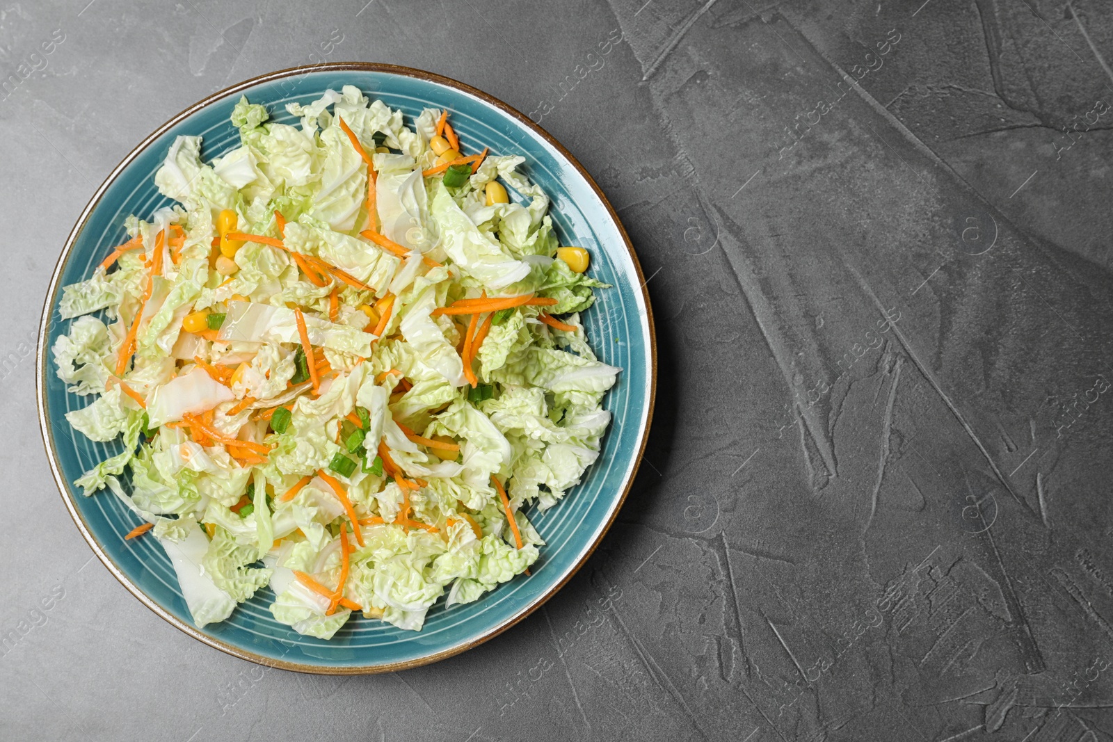 Photo of Plate of fresh cabbage salad with carrot on grey table, top view. Space for text