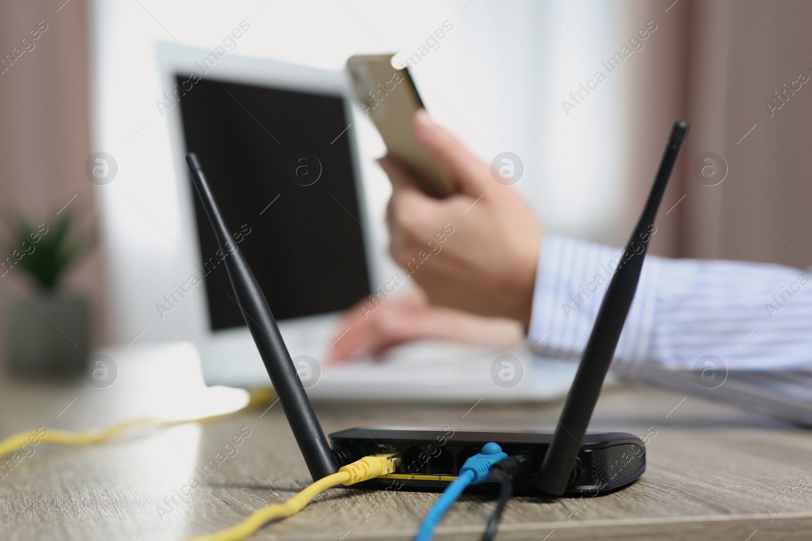 Photo of Woman with smartphone working on laptop at table indoors, focus on Wi-Fi router