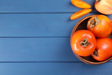 Photo of Delicious ripe persimmons on blue wooden table, top view. Space for text