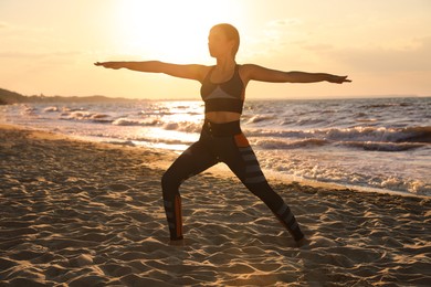 Image of Young girl doing yoga on beach at sunset