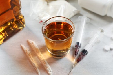 Photo of Alcohol and drug addiction. Whiskey in glass, syringes and cocaine on white table, closeup