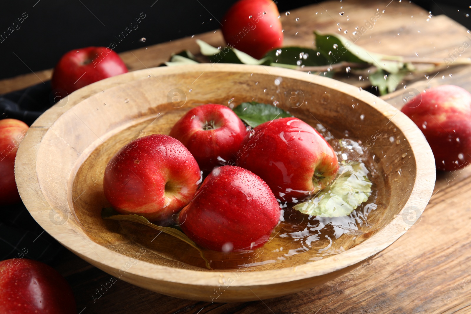 Photo of Ripe red apples in bowl of water on wooden table